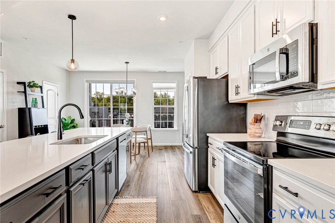 Contemporary kitchen featuring a large island with an undermount sink, white countertops, stainless steel appliances, white subway tile backsplash, and wood-finish flooring