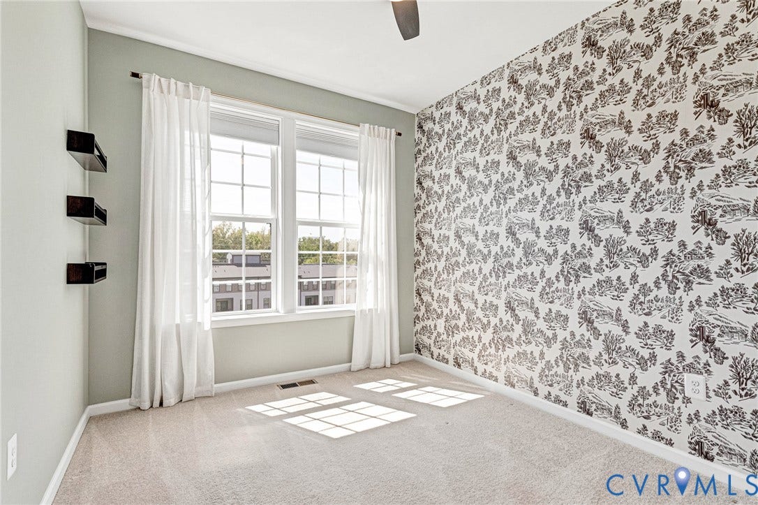 Wall-to-wall carpeting, dual windows with curtains, accent wallpaper, and a ceiling fan