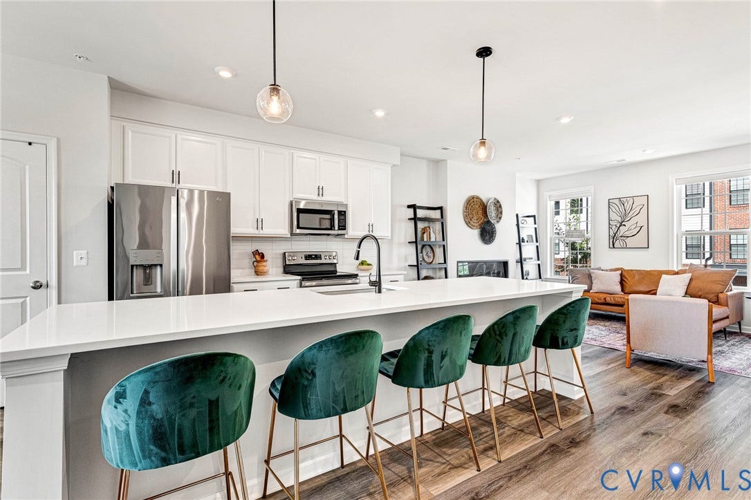 Open-concept living area featuring a kitchen island, white cabinetry, stainless steel appliances, and wood-finish flooring