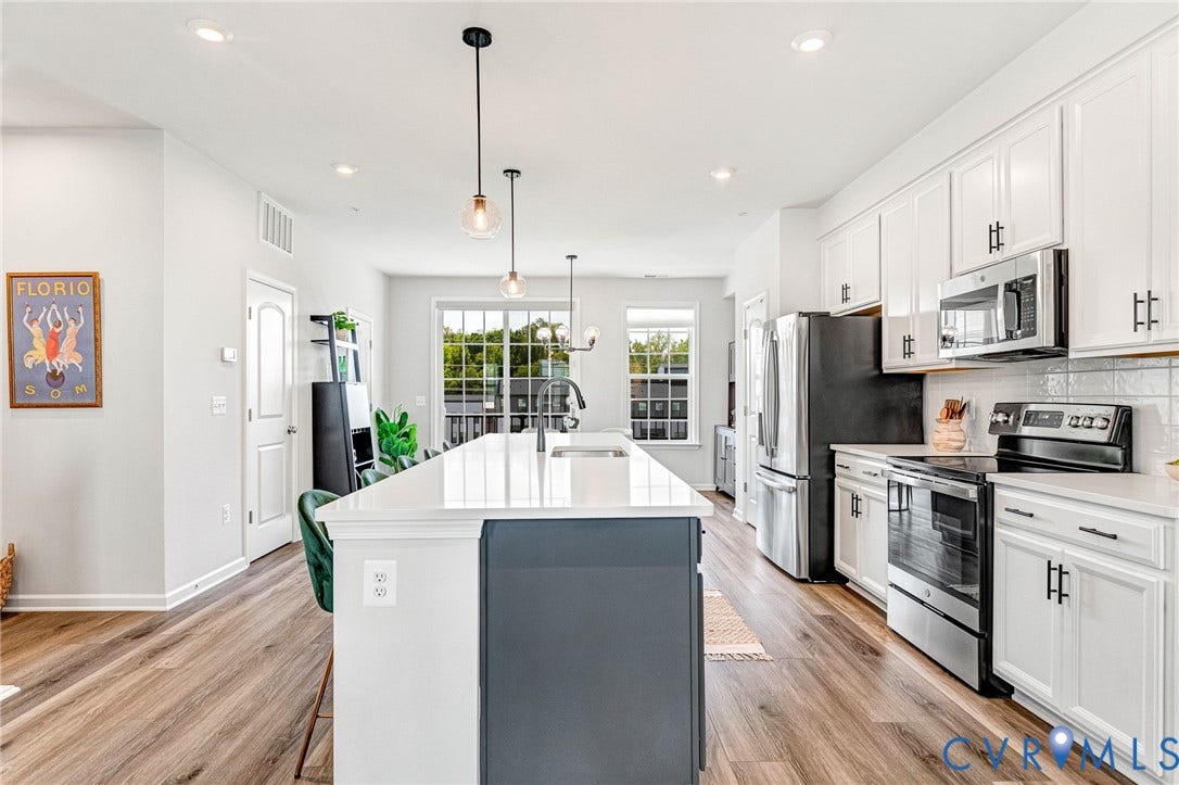 White cabinetry with matte black hardware, stainless steel appliances, kitchen island with integrated sink, wood-finish flooring, and recessed lighting