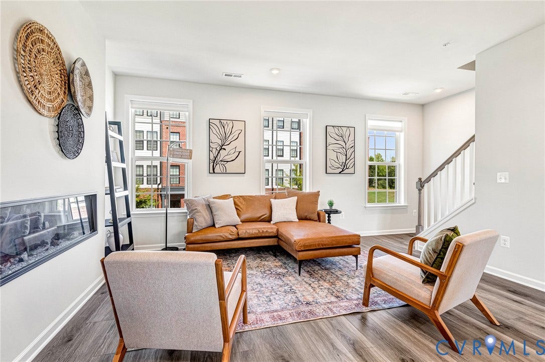 Spacious living area featuring wood-finish flooring, multiple windows, a linear fireplace, and a staircase with white balusters