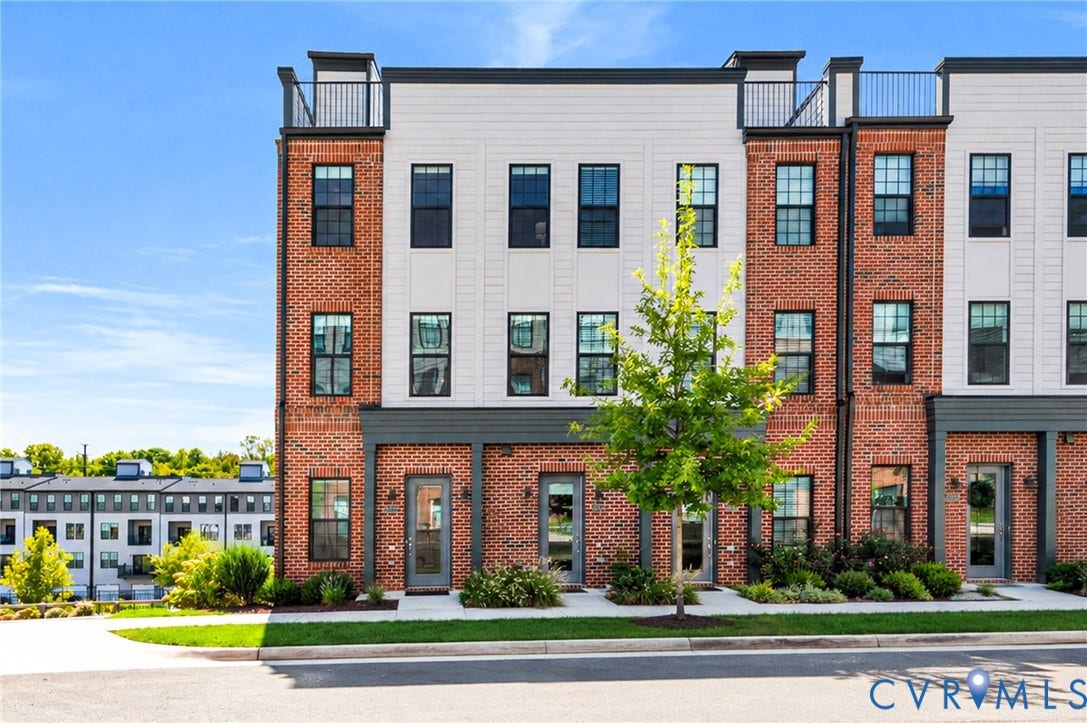 Brick and siding exterior with multiple windows, black-framed windows, dark gray front doors, and integrated landscaping