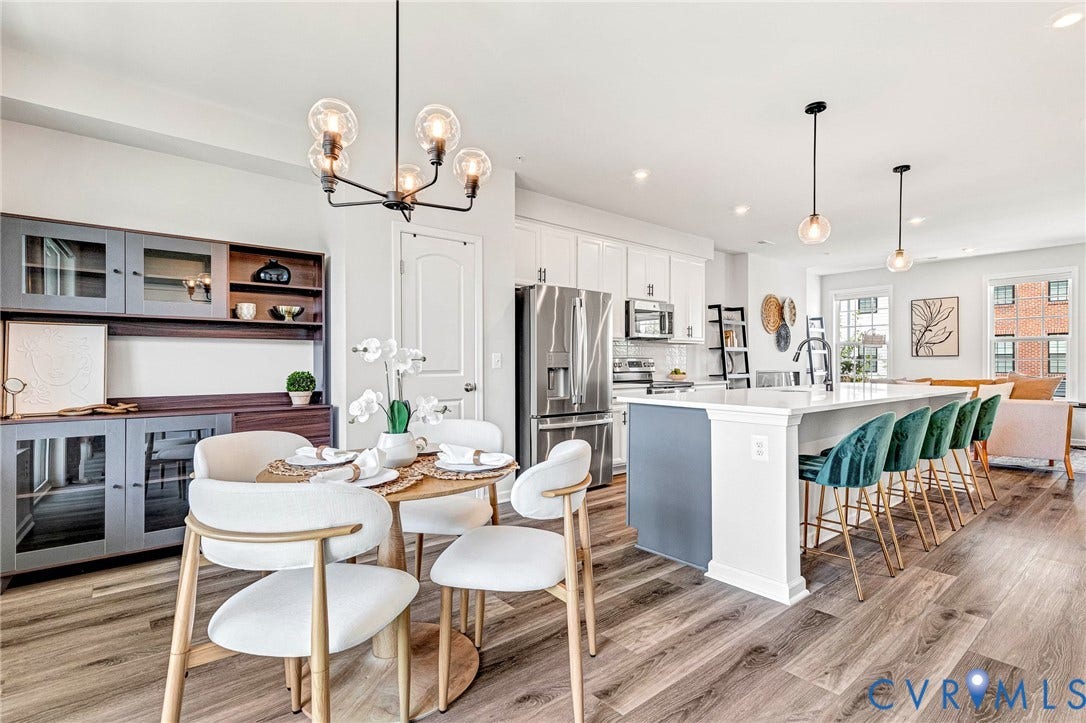 Open-concept layout featuring wood-finish flooring, a white kitchen with stainless steel appliances, a large center island with seating, and a built-in hutch with glass-front cabinetry