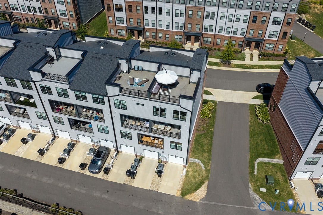 Multi-story townhome featuring a private rooftop deck, multiple balconies with metal railings, individual garage bays, and dedicated driveways