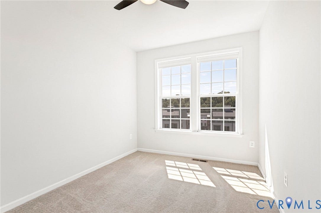 Windowed room with light-colored carpeting, a ceiling fan, and two large windows with blinds