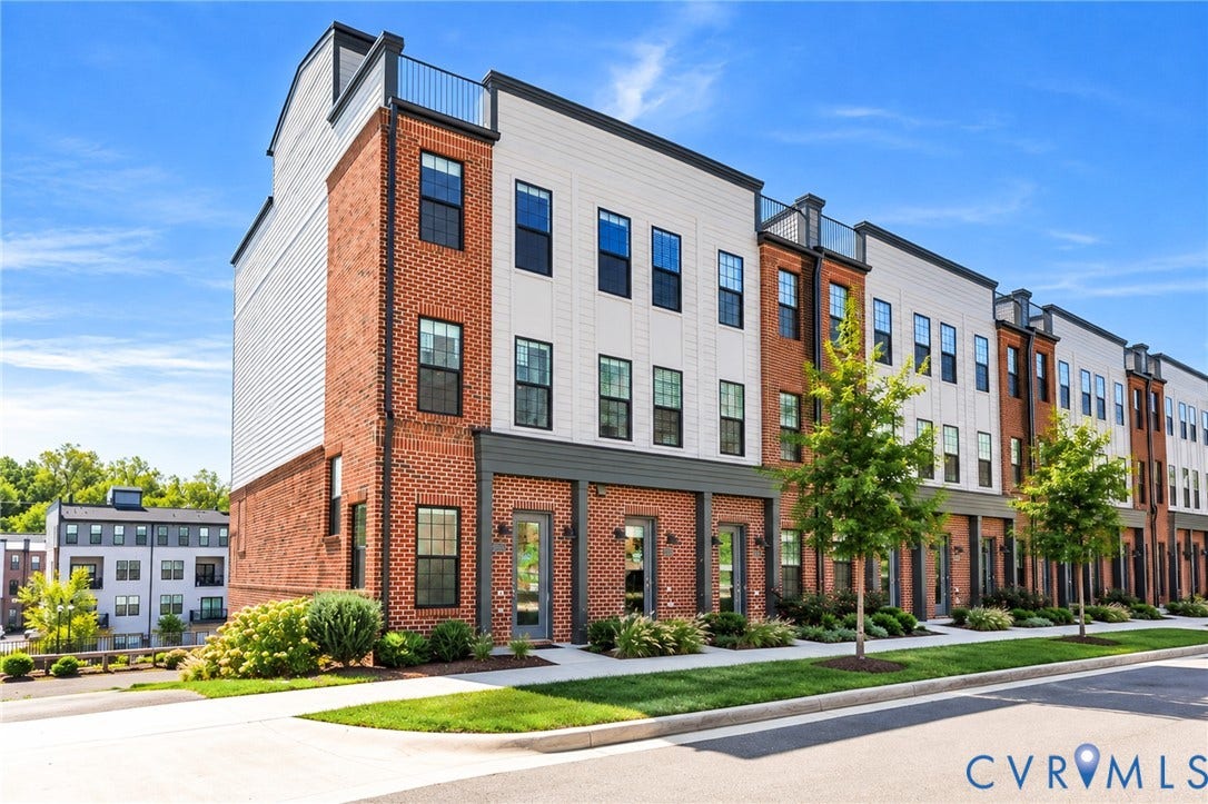 Multi-story townhome exterior featuring brick and horizontal siding, rooftop terrace with metal railing, and ground-level entry doors