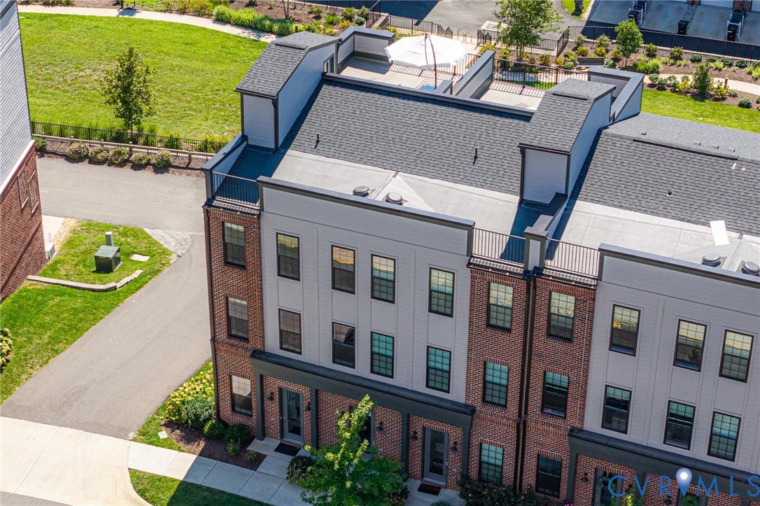 Modern townhome elevation featuring brick and light-colored siding, black-framed windows, a flat roofline with a visible rooftop terrace, and a dark asphalt shingle roof