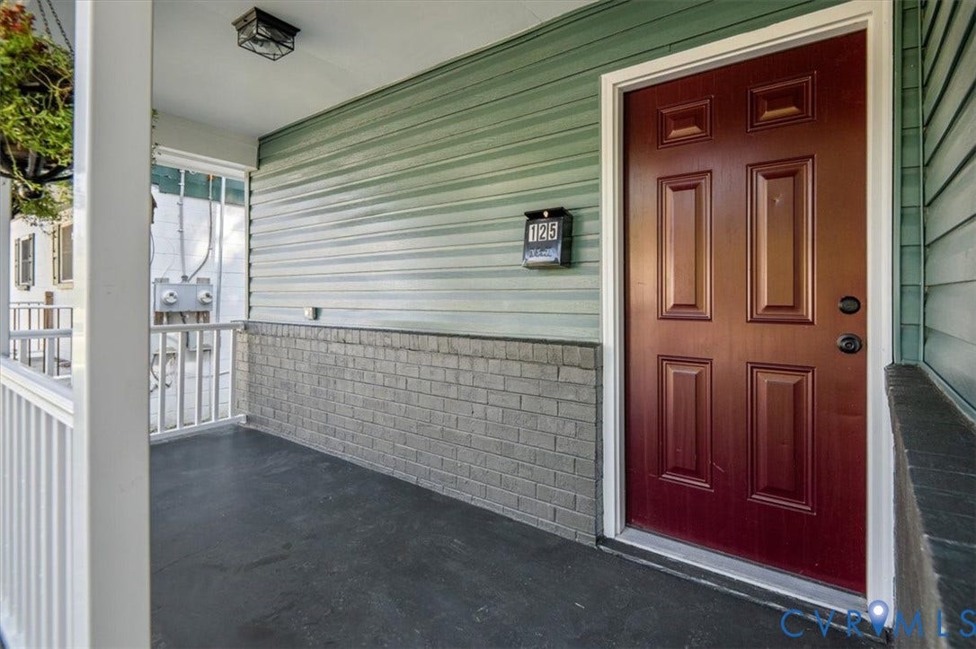 Covered front porch featuring a paneled entry door, horizontal siding, and a brick-finish base