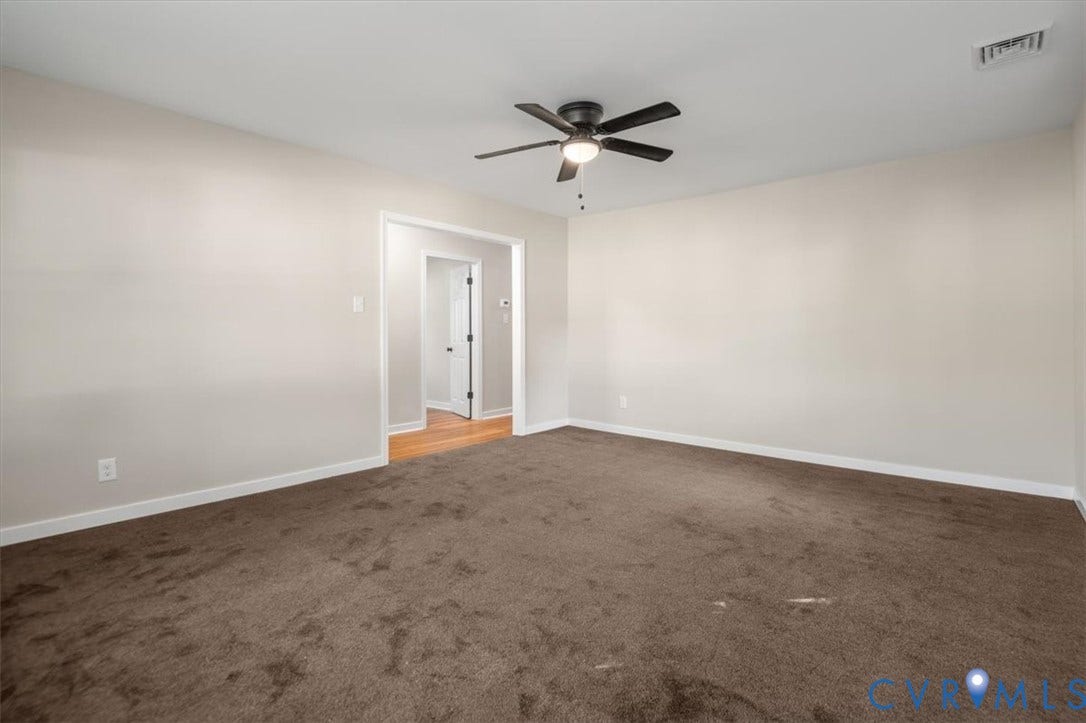 Spacious room with plush brown carpeting, light neutral wall tones, a modern ceiling fan with integrated lighting, and a doorway leading to a separate area with wood-finish flooring