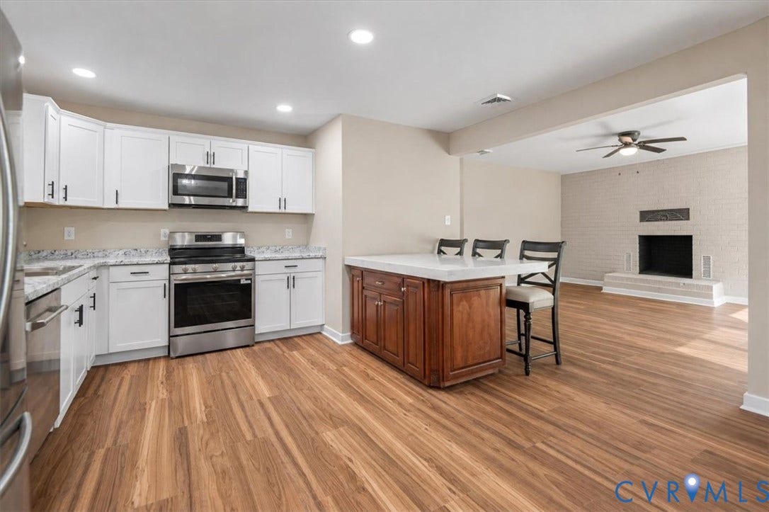 Kitchen featuring wood-finish flooring, white cabinetry, stainless steel appliances, and an island with seating
