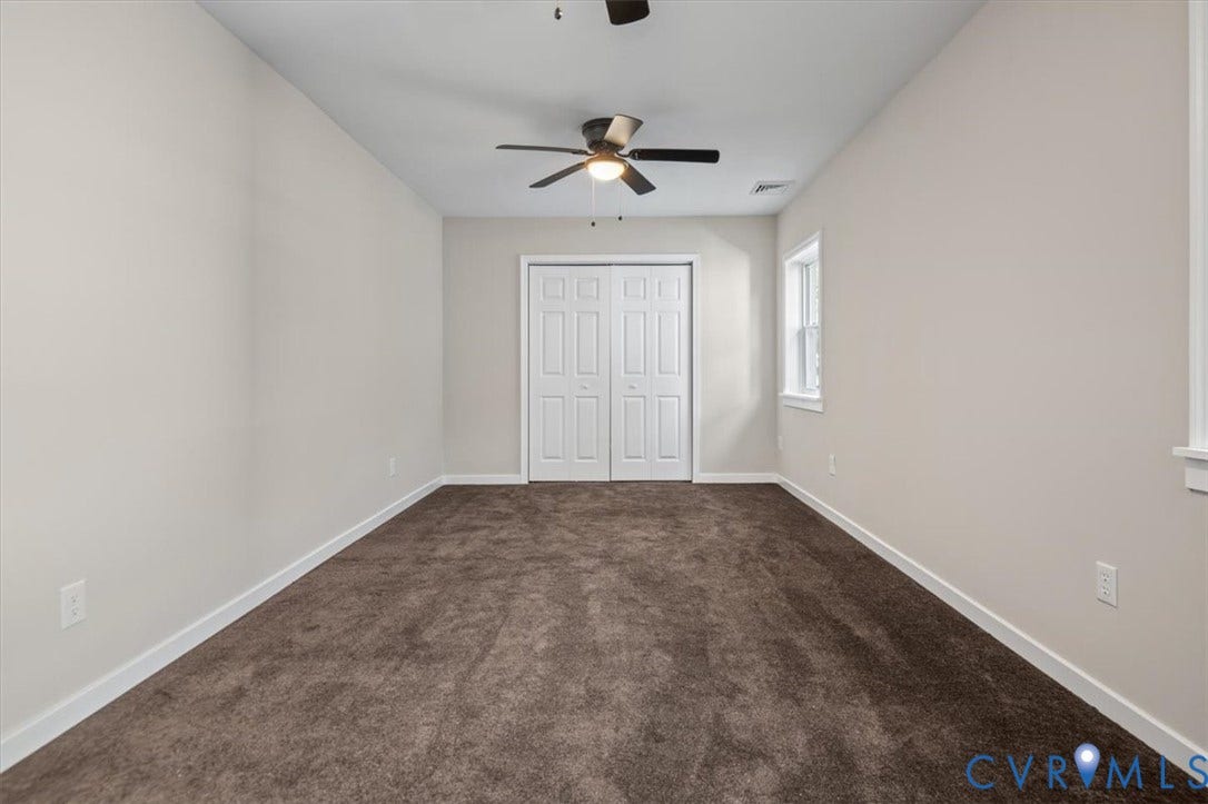 Neutral tone wall paint, brown carpet flooring, ceiling fan with light fixture, double bifold closet doors, and a single window