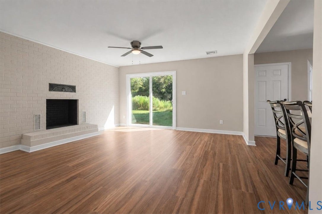 Wood-finish flooring, brick fireplace with mantel, ceiling fan with integrated lighting, sliding glass door, and a partially visible white paneled door