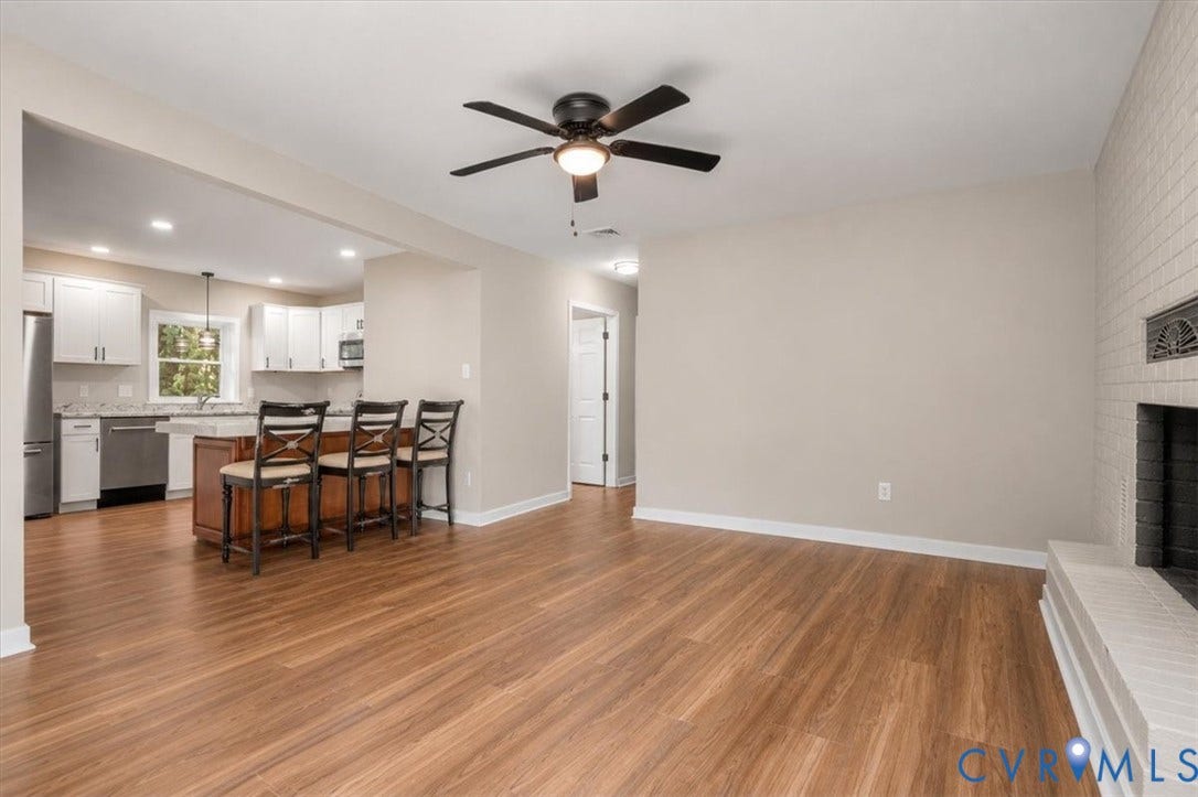 Open-concept living area with wood-finish flooring, a ceiling fan, and a white brick fireplace