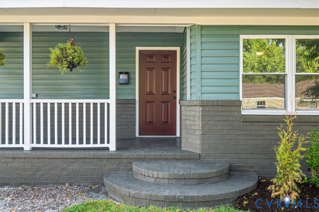 Front entrance with a deep brown door, white window trim, and light blue siding