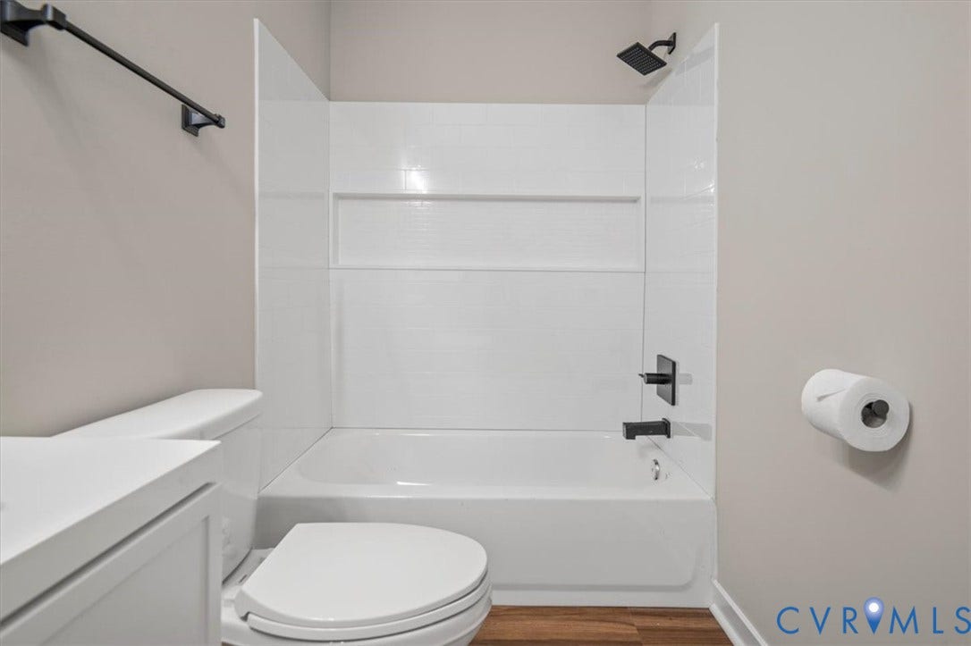 White bathtub with black-finish shower fixtures, white shower surround, and wood-finish flooring