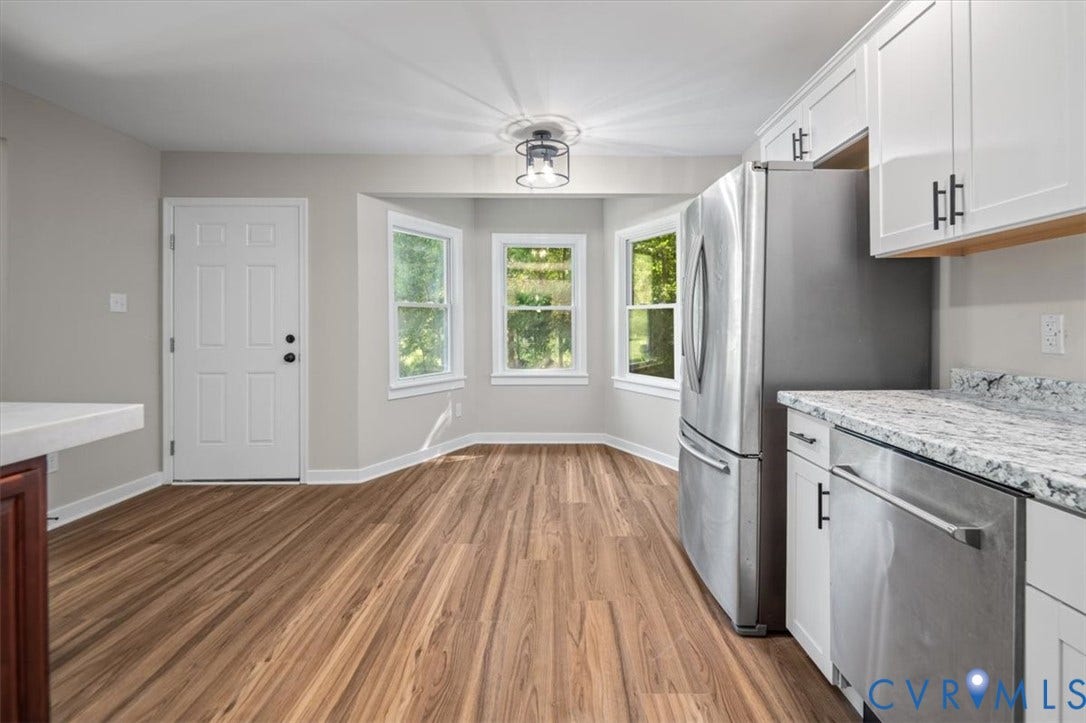 Wood-finish flooring, white cabinetry with black hardware, stainless steel refrigerator and dishwasher, light-toned countertops, and a bay window
