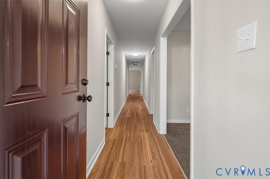 Panel door with black hardware, wood-finish flooring, recessed lighting, neutral wall tones, and white trim
