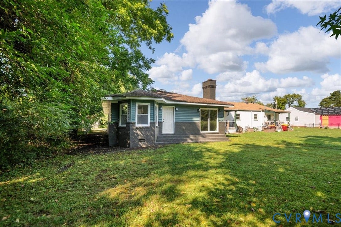 Expansive rear lawn featuring mature trees, a multi-pane glass sliding door, and a chimney