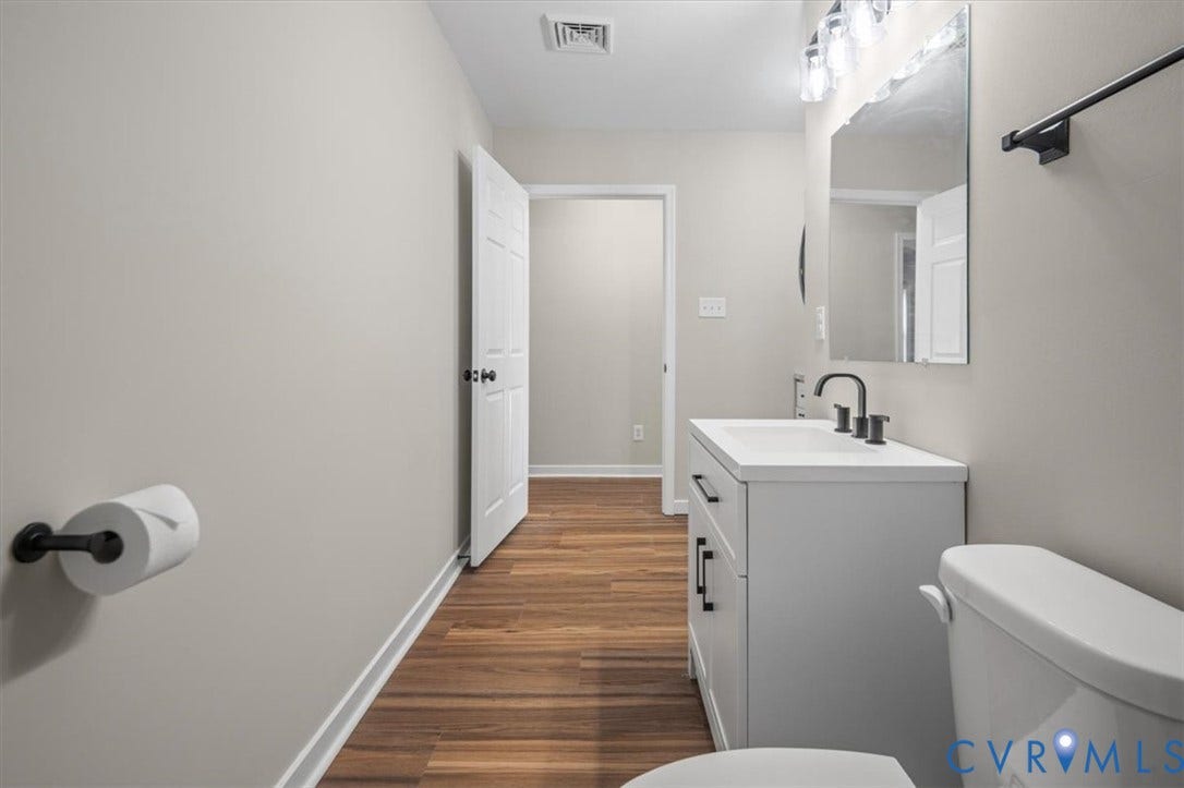 Bathroom featuring wood-finish flooring, a white vanity with black hardware, a black faucet, and a wall-mounted mirror with integrated lighting