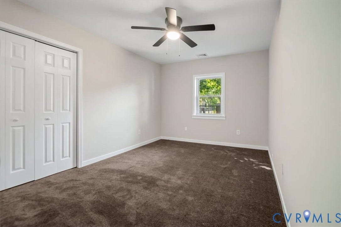 Neutral tone wall paint, carpet flooring, ceiling fan, and a single window with white trim