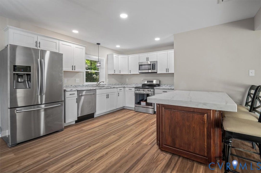Kitchen featuring wood-finish flooring, white cabinetry, stainless steel appliances, and a central island with a light-toned countertop