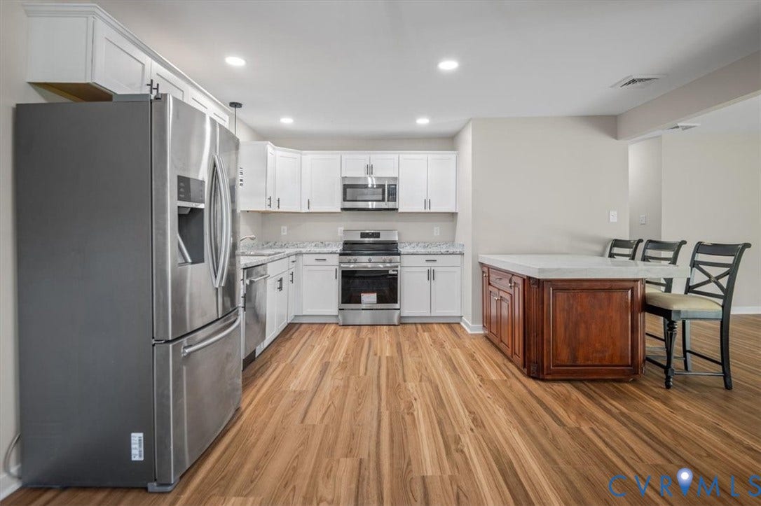 Modern kitchen featuring wood-finish flooring, white cabinetry, stainless steel appliances, and a central island with a light-toned countertop
