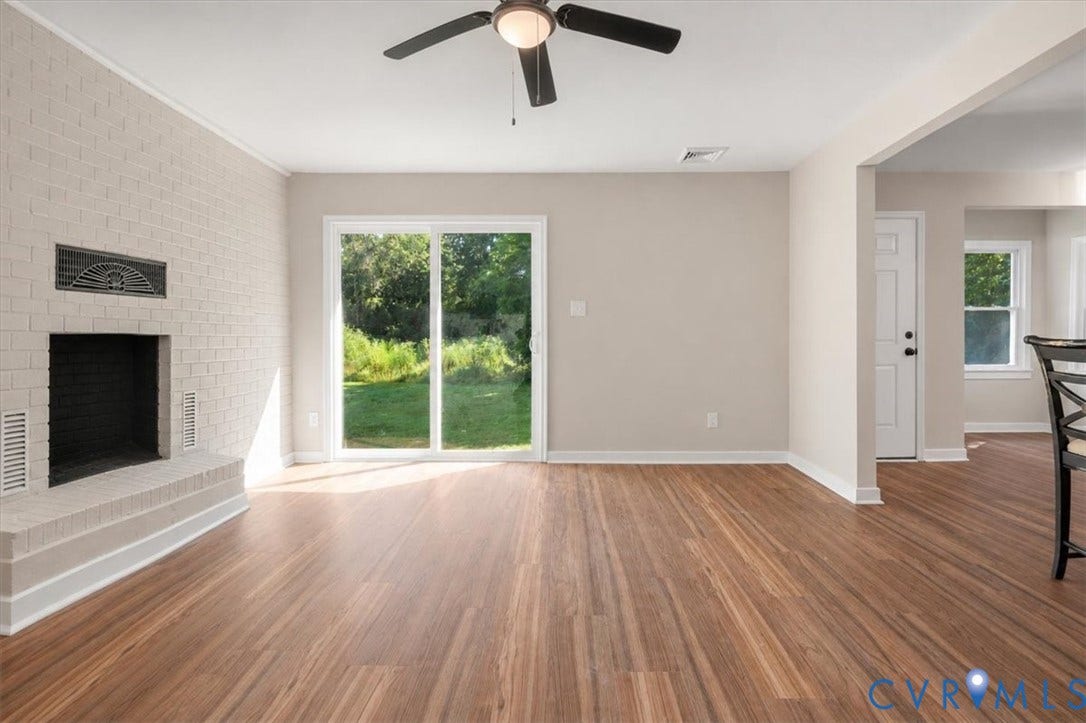 Wood-finish flooring, brick fireplace, sliding glass door, ceiling fan, and white trim