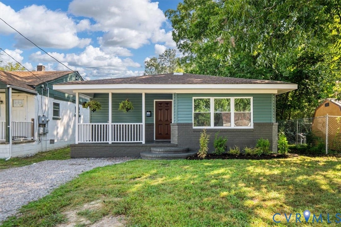 Mint green siding with a dark brown front door, white porch railing, and a gravel driveway
