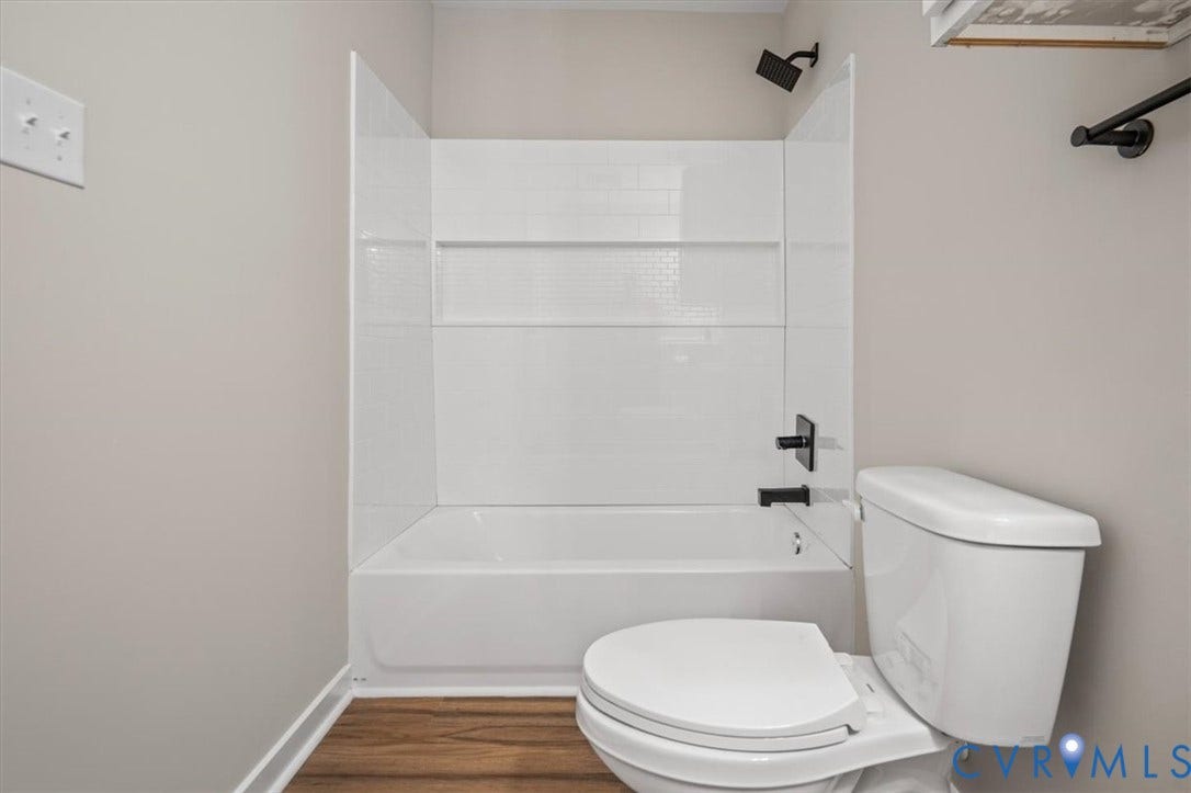 Tub/shower combination featuring white subway tile surround, matte black fixtures, and wood-finish flooring