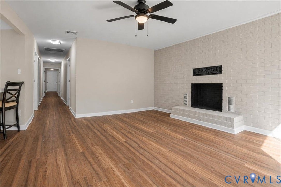 Wood-finish flooring throughout, painted brick fireplace with hearth, ceiling fan with integrated lighting, recessed lighting, and a neutral color palette