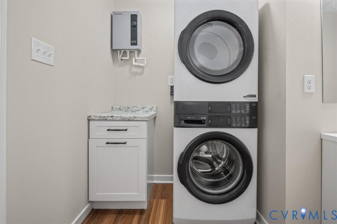 Stackable laundry appliances, white cabinetry, a stone-finish countertop, and wood-finish flooring