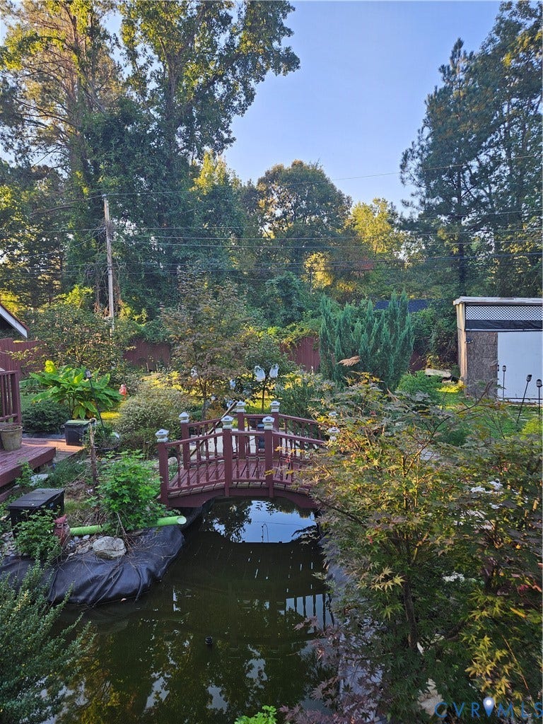 Expansive backyard featuring a pond with a decorative footbridge, mature trees, and established landscaping
