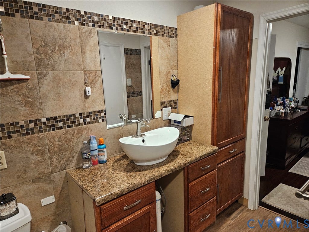 Vanity with a vessel sink, a granite-finish countertop, and wood-finish cabinetry
