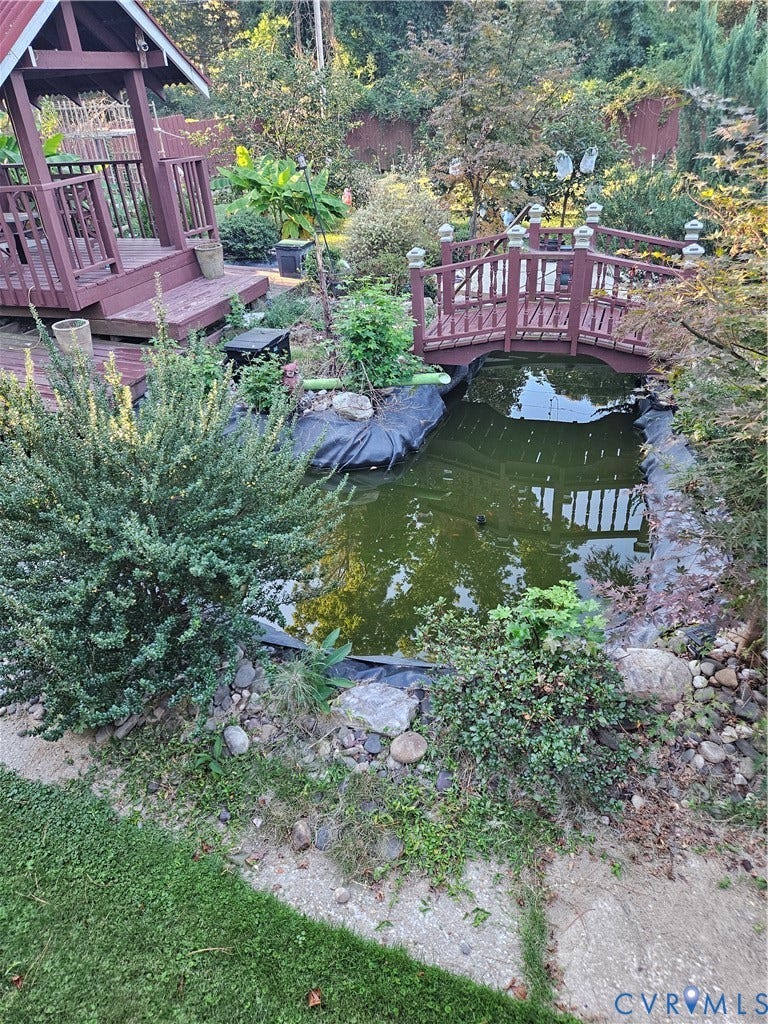 Expansive outdoor space featuring a wooden gazebo, a decorative footbridge, and a pond surrounded by lush landscaping