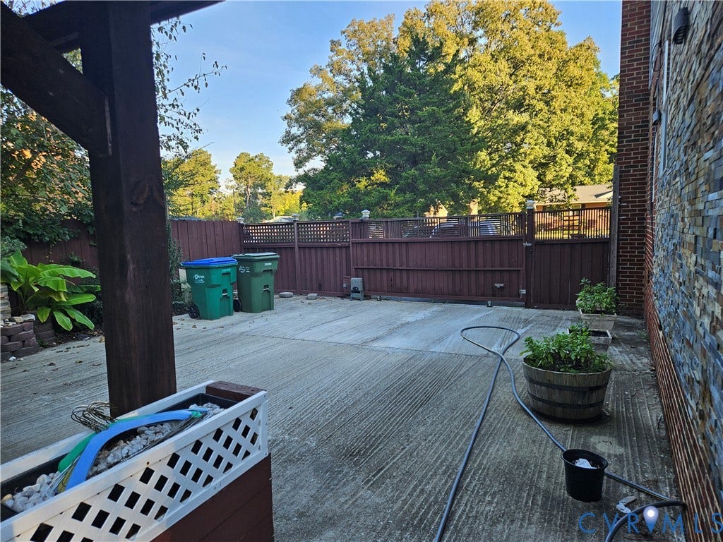 Paved outdoor area with a durable privacy fence, complemented by a stone-clad exterior wall and a structural pergola element