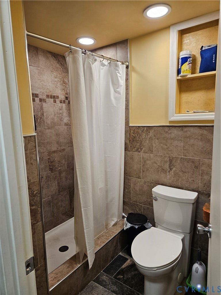 Tiled shower enclosure with built-in shelving, complemented by recessed lighting and a white toilet