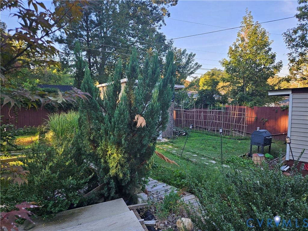 Expansive yard featuring mature trees, a wooden privacy fence, and a garden structure