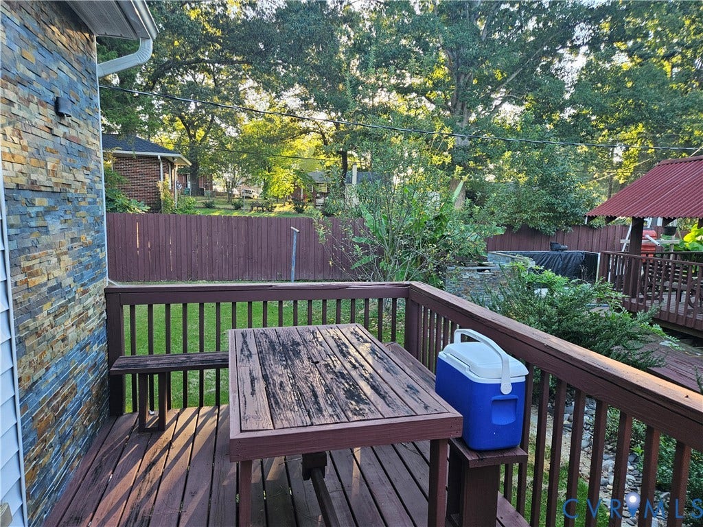 Wood deck with integrated seating, stone veneer exterior siding, wood privacy fence, and mature trees