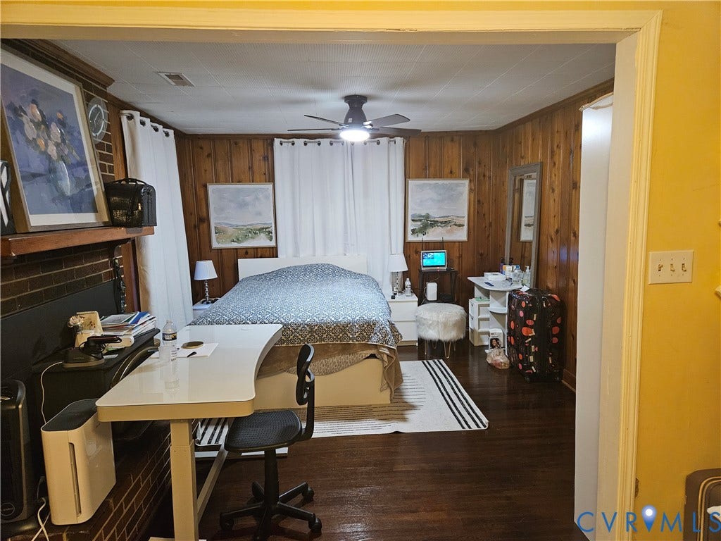 Wood-paneled walls, dark wood-finish flooring, ceiling fan, and a painted brick fireplace