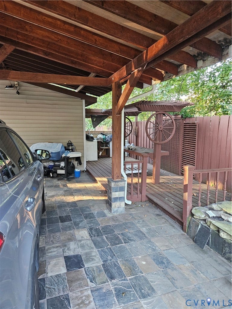 Covered outdoor area featuring a wood-beam ceiling, stone-tile flooring, wood deck, and a wood privacy fence