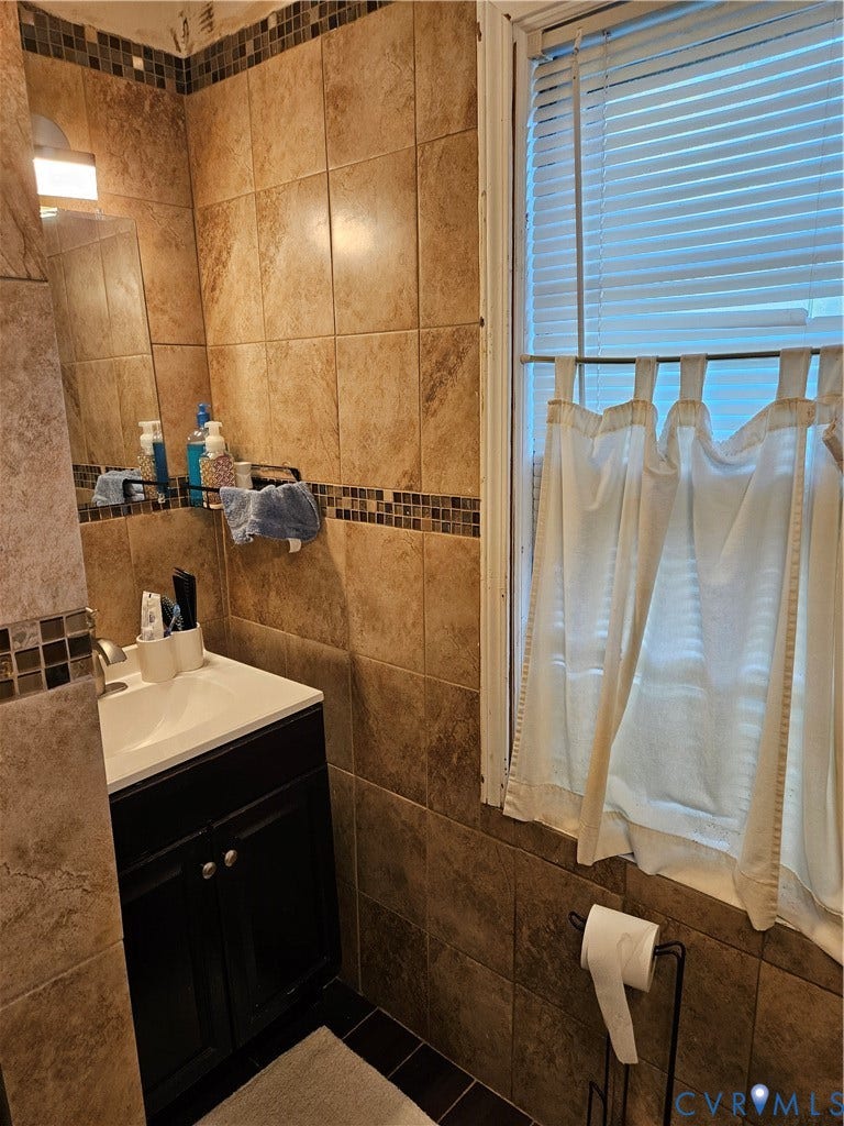 Full-height wall tiling with mosaic accent band, dark wood-finish vanity with countertop basin, and contrasting floor tiles