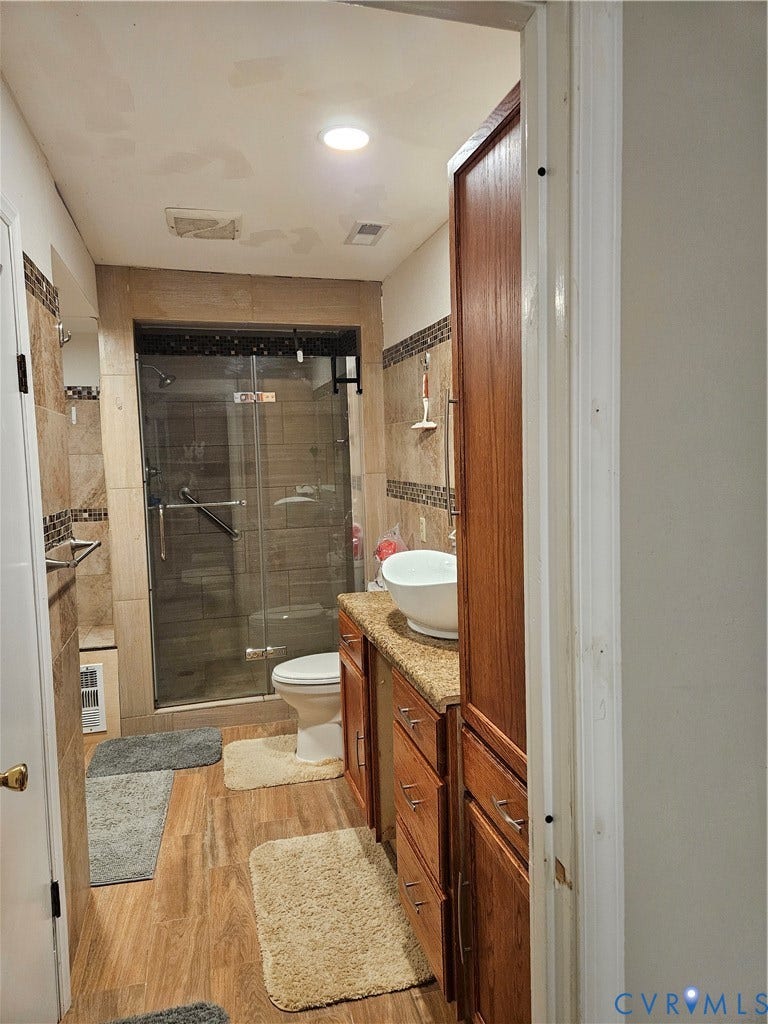 Bathroom featuring a glass-enclosed shower, wood-finish flooring, a vanity with a bowl sink, and built-in wood cabinetry