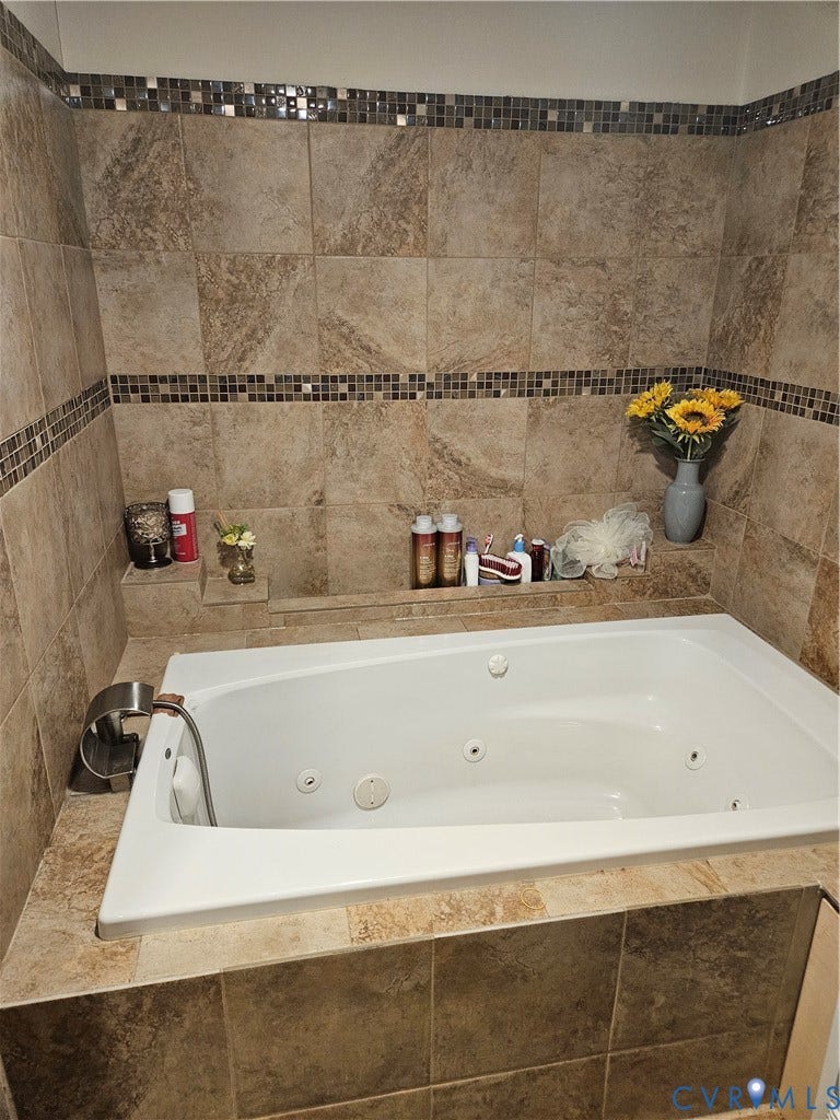 Built-in jetted tub with tile surround, complemented by a tiled wall with mosaic accent bands and integrated shelving