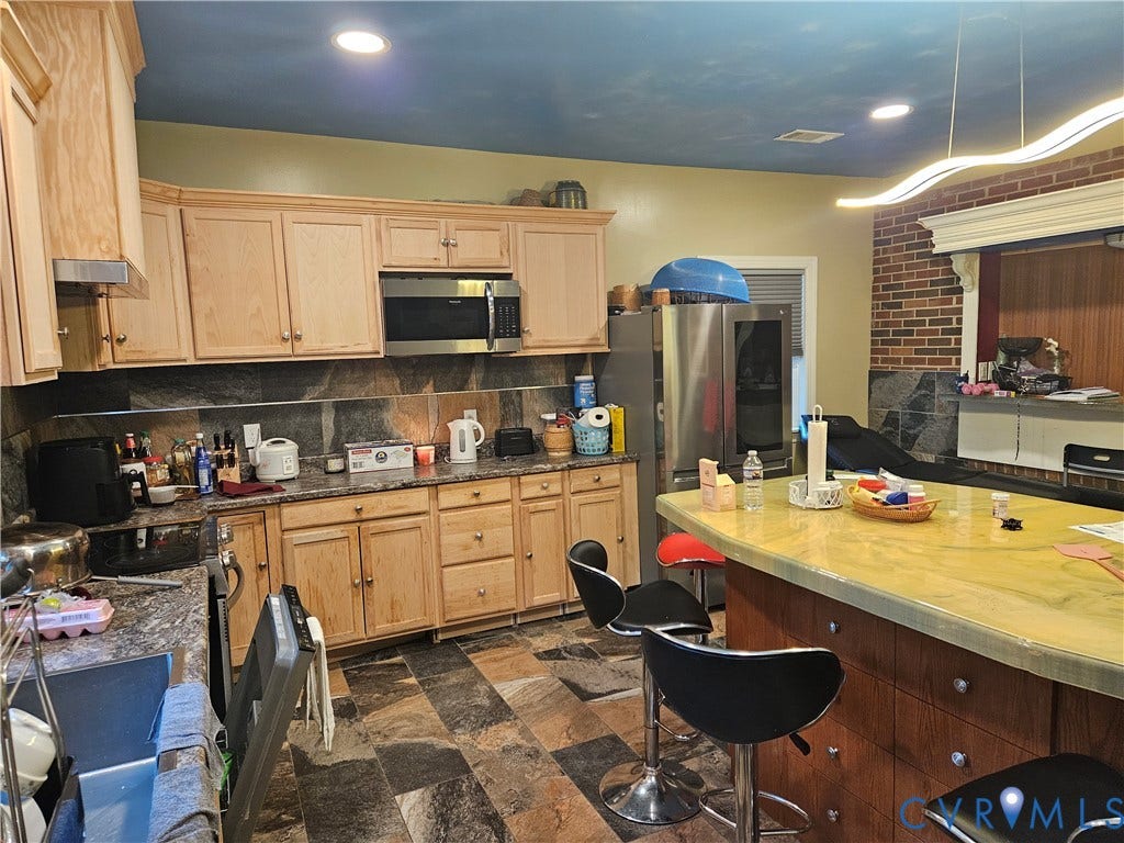 Kitchen featuring wood cabinetry, stainless steel appliances, stone-finish backsplash, and multi-tone flooring