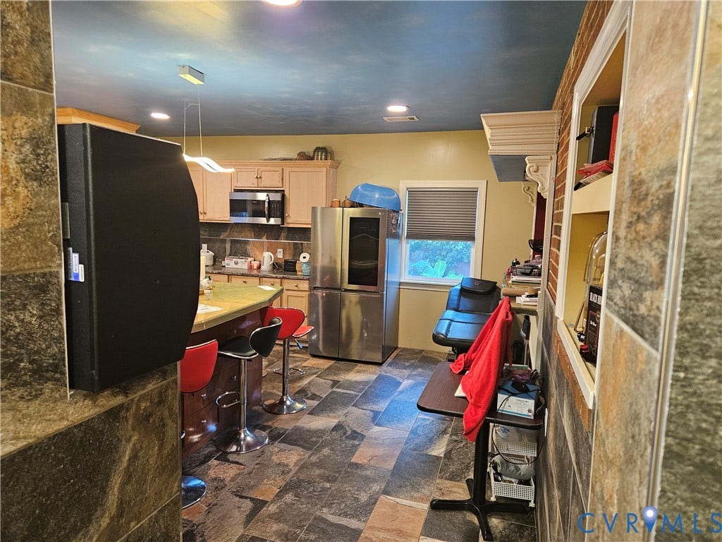 Kitchen featuring slate-style flooring, light wood-finish cabinetry, stainless steel appliances, and a curved island with countertop