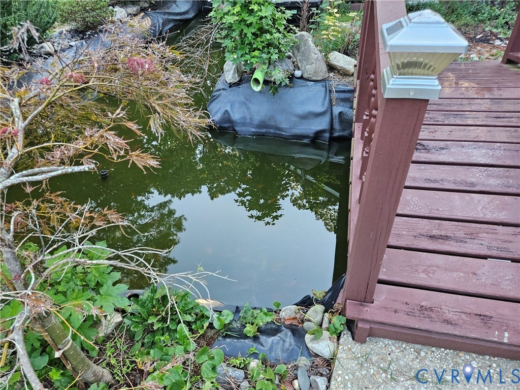 Pond feature with surrounding natural landscaping, dark wood bridge, and a solar-powered post cap light