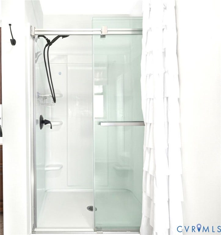 Shower enclosure with sliding glass doors, matte black shower fixtures, and integrated shelving