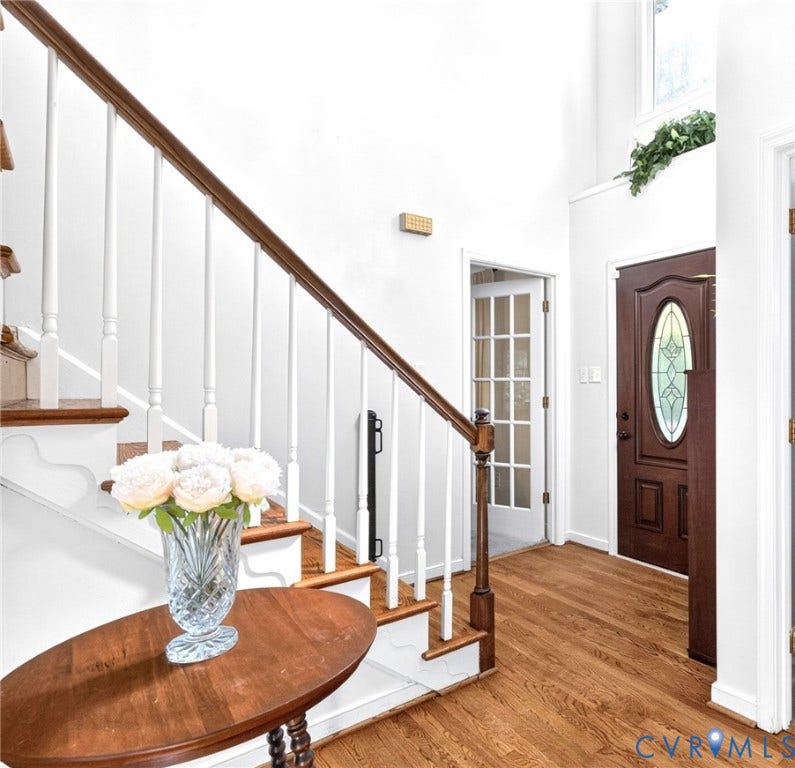 Two-story foyer featuring hardwood floors, a staircase with white balusters and wood handrail, a paneled front door with oval stained-glass insert, and a French door with multiple glass panes leading to the Living Room/Office