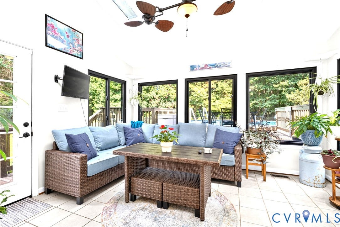 Sunroom featuring light-colored tile flooring, multiple windows with black framing, and a ceiling fan