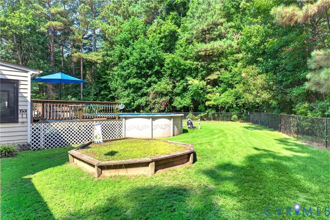 Expansive backyard featuring a lush lawn, above-ground pool, and wood deck with lattice skirting